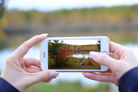 A young woman shoots a landscape on a smartphone. Outdoor shooting in nature. Shallow depth of field.の写真素材
