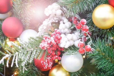 Decorated Christmas tree closeup. Rowan berries, red and golden balls and illuminated garland with flashlights. New Year baubles macro photo with bokeh. Winter holiday light decoration.の写真素材