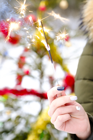Close-up of a womans hand holding a Bengal lights against the background of the Christmas tree with a shallow depth of field.の写真素材