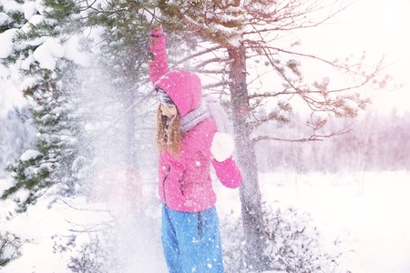 Beautiful happy laughing red-haired young woman in a winter tracksuit covered in snow flakes. Winter forest landscape background.の写真素材