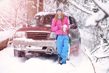 Beautiful happy smiling red-haired young woman in a winter tracksuit next to an SUV. Winter forest. Landscape.の写真素材