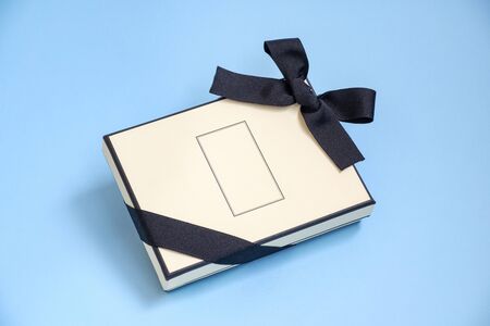 Gift box with colored ribbon as a gift for Christmas, New Year, Mothers Day, anniversary, birthday, party, isolated on a blue background, top view. Gift to a colleague at workの写真素材