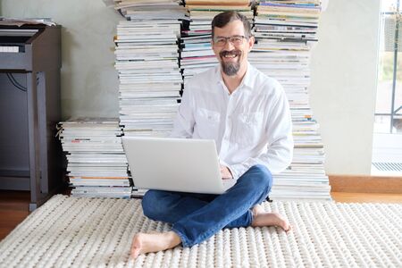 Male architect in a white shirt works at a laptop, smiling. Sits on the floor.の写真素材