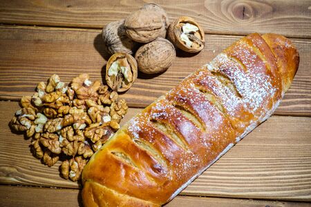 Fresh roll with walnuts and icing sugar on a wooden background. Sweet dessert with nuts on an old table.の写真素材
