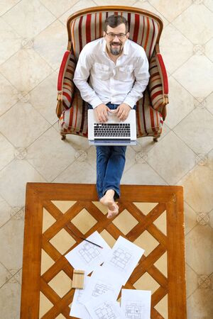 Male architect in a white shirt works at a laptop, smiling. Sits on the floor.の写真素材