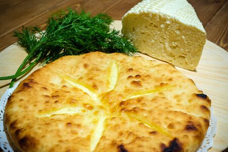 Ossetian pie with cheese and dill. A traditional dish of the Caucasian fish soup. Dough product with filling on the background of an old wooden table. The concept of tasty and healthy food.の写真素材