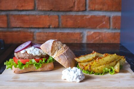 Homemade burger with beef chop, tomato, lettuce and dorblu blue cheese sauce. Serve on a wooden kitchen board on a table made of natural stone. Background image.の写真素材