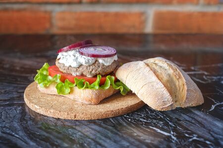 Homemade burger with beef chop, tomato, lettuce and dorblu blue cheese sauce. Serve on a wooden kitchen board on a table made of natural stone. Background image.の写真素材