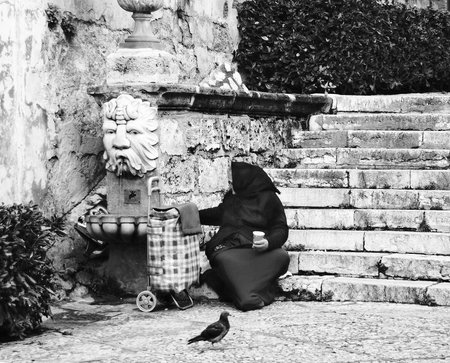 A homeless beggar sits on the steps of the old city. Black and white.の写真素材