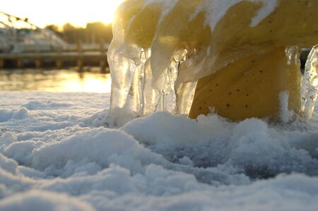 Icicles on yellow mooring bollard in port. Winter by the sea.の写真素材