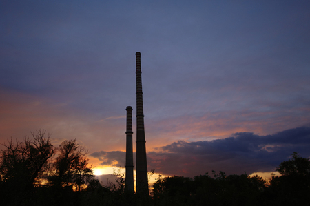 Old concrete high chimneys on cloudy sunset sky. Cause of global warming.の写真素材