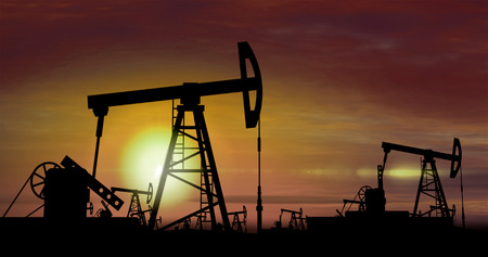 Oil pumps silhouettes working on clouds and sun in background. Pumpjack on oilfield on sunset. Concept of oil rig, global warming, environment pollution and fossil fuels.の写真素材