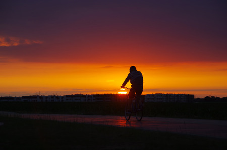 Silhouette of Man on bicycle with city and nice sunset in backgroundの写真素材