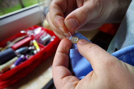 Needle and thread in the tailor hand. Manual sewing on the shirt button. Handmade work.