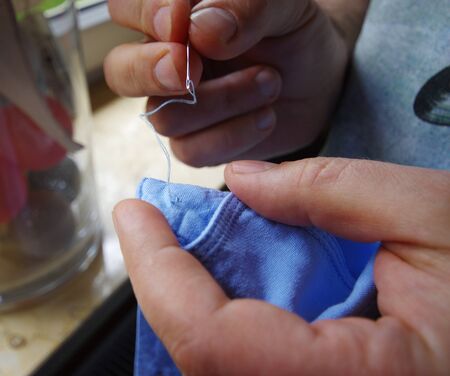 Needle and thread in the tailor hand. Manual sewing on the shirt button. Handmade work.