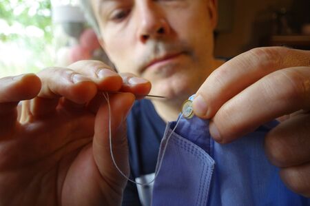 Tailor man with needle and thread in the hand. Handmade work. Manual sewing on the shirt button....