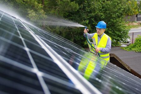 Man cleans solar panel on the roof. Maintenance of renewable energy in a private home. Worker washes the solar installation with water.の写真素材
