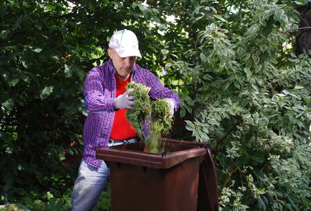 Green waste segregation. A gardener throwing green hay into a bio recycling brown bin. Ecology and...