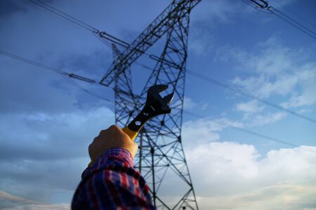 Industry and power line maintenance concept. Wrench in hand with silhouette of electric pylon in...