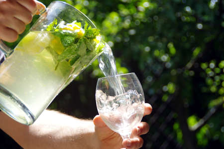 A cold lemon drink with citrus slices poured from a jug into a glass. Cool and fresh homemade...
