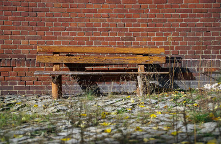 Old brown bench with brick wall in background. Vintage place for rest. Empty wooden and weathered seat in forgotten exterior.の写真素材