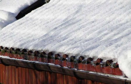 Snow in the gutter during the winter season. Snowy cover on the roof of the house. Sunny cold day.