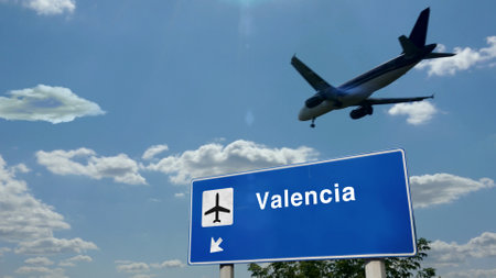 Airplane silhouette landing in Valencia, Spain. City arrival with international airport direction signboard and blue sky. Travel, trip and transport concept 3d illustration.の写真素材
