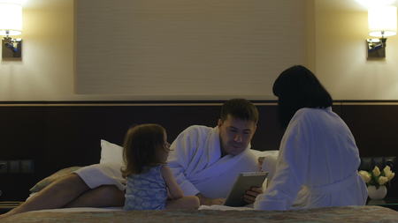 Father with a small child and his wife play with the phone in bedの写真素材