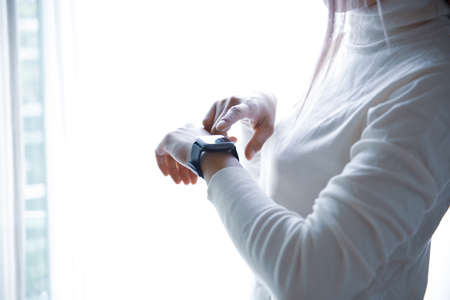 A woman's hand in white clothes, operating a smartwatch with a white backgroundの写真素材