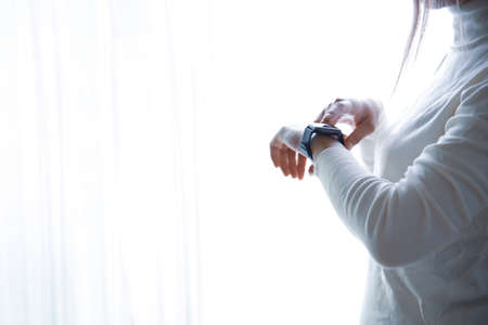 A woman's hand in white clothes, operating a smartwatch with a white backgroundの写真素材