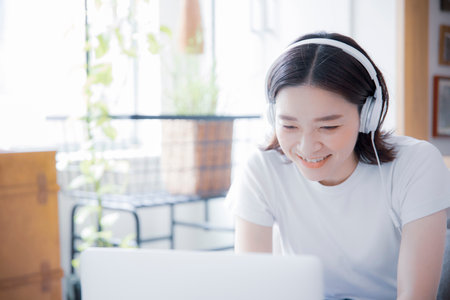 Japan woman working remotely in a well-lit room with earphones and laptop phones for online classes...
