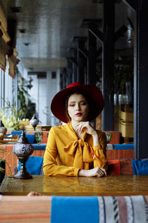 sad girl in a yellow dress and a hat sits in a cafe, pandemic, isolation.