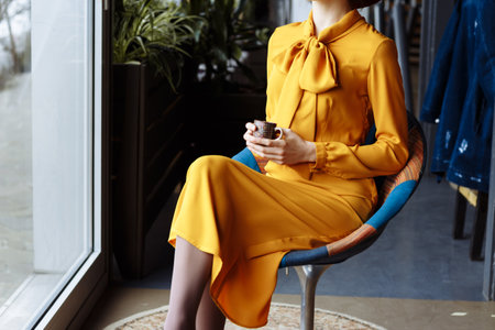 girl in a cafe with a cup of coffee and a hat. beautiful girl with a cup of coffee at the window in a cafe, waiting for a meeting, breakfastの写真素材