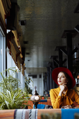girl in a cafe with a cup of coffee and a hat. beautiful girl with a cup of coffee at the window in a cafe, waiting for a meeting, breakfastの写真素材