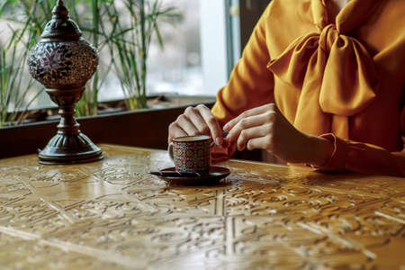 girl in a cafe with a cup of coffee and a hat.portrait of sensual young girl wearing floppy hat and blouse with bow. Beautiful brunette woman in cafe holding cup of coffeeの写真素材