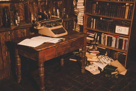 old typewriter is on the table next to the book lies and is a cup.old books are on the shelves. Vintage room of the researcher, critic, scientist,の写真素材