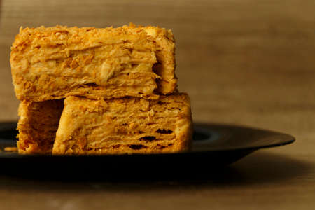 Slice of orange cake on black plate on the wooden table, food background. Napoleon