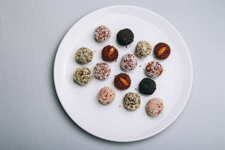 sweets from dried fruits with nuts and sesame seeds Tasty energy balls with dried fruits and nuts in coconut chips on a white plateの写真素材