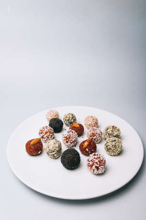sweets from dried fruits with nuts and sesame seeds Tasty energy balls with dried fruits and nuts in coconut chips on a white plateの写真素材