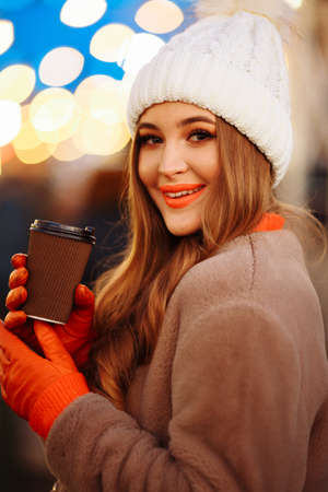 beautiful girl on the background of lights with coffee, on the street, holiday, new year. a walk through the evening city smilesの写真素材