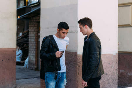 beautiful and attractive guy is standing in the city, posing. dressed in a black leather, white T-shirt, jeans and white shoes. walk around the city in black glasses. communication. meeting friends.の写真素材