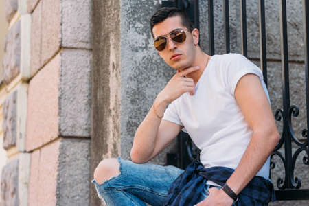Attractive, sexy guy sits on the street in sunglasses. self-confidence, flatulence and arrogance. model, posing, portrait of a young manの写真素材