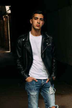 young, handsome guy in a white T-shirt, black, leather jacket and blue, torn jeans is on the street, model, city walk, live style.in white sneakersの写真素材