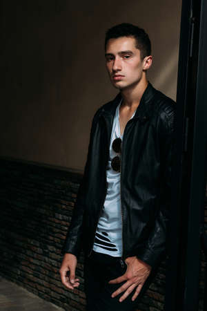 young, handsome guy in a white T-shirt, black, leather jacket and black pants is on the street, n...