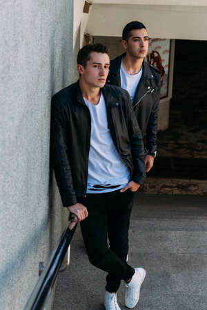 expectation Sexy mans posing near railing. an attractive young mans In a black leather jackets, a white T-shirts and white sneakers is standing near the railing. friendship. two models. showing clothesの写真素材