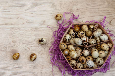 a lot of quail eggs lies in the basket that stands on the violet decor, on the table