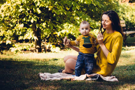 Happy young mother playing with baby in autumn park with yellow maple leaves.Family walking outdoors in autumn. Little boy with her mother playing in the park in autumn.の写真素材