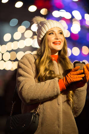 beautiful girl on the background of lights with coffee, on the street, holiday, new year. a walk through the evening city smilesの写真素材