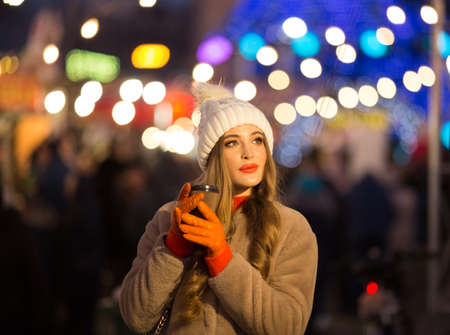 beautiful girl on the background of lights with coffee, on the street, holiday, new year. a walk through the evening city smilesの写真素材