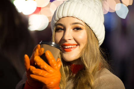 beautiful girl on the background of lights with coffee, on the street, holiday, new year. a walk through the evening city smilesの写真素材